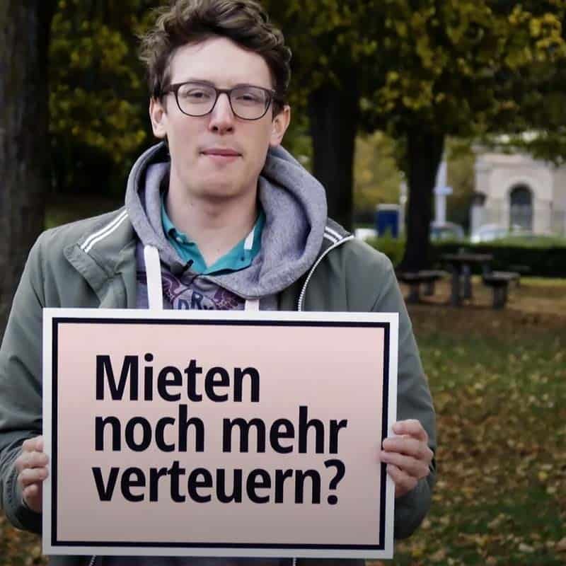 Junger Mann hält Schild auf dem steht «Mieten noch mehr verteuern?»