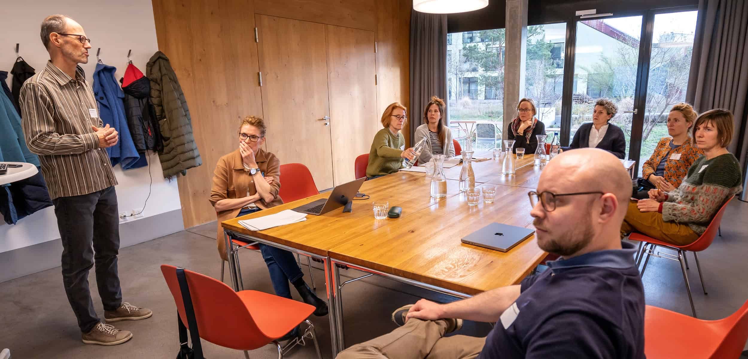 Intervisionsgruppe Wohnbaugenossenschaften: Menschen sitzen um einen grossen Tisch und lauschen einem Vortrag